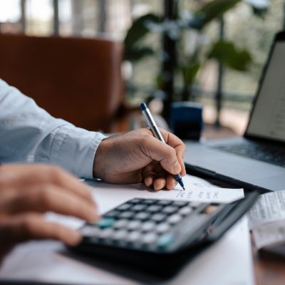 A person calculating finances with a calculator and pen on a desk indoors.