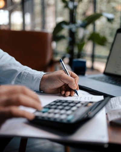 A person calculating finances with a calculator and pen on a desk indoors.